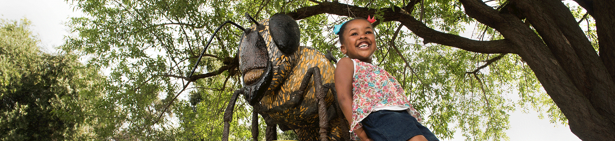 bee statue in garden with child smiling on it